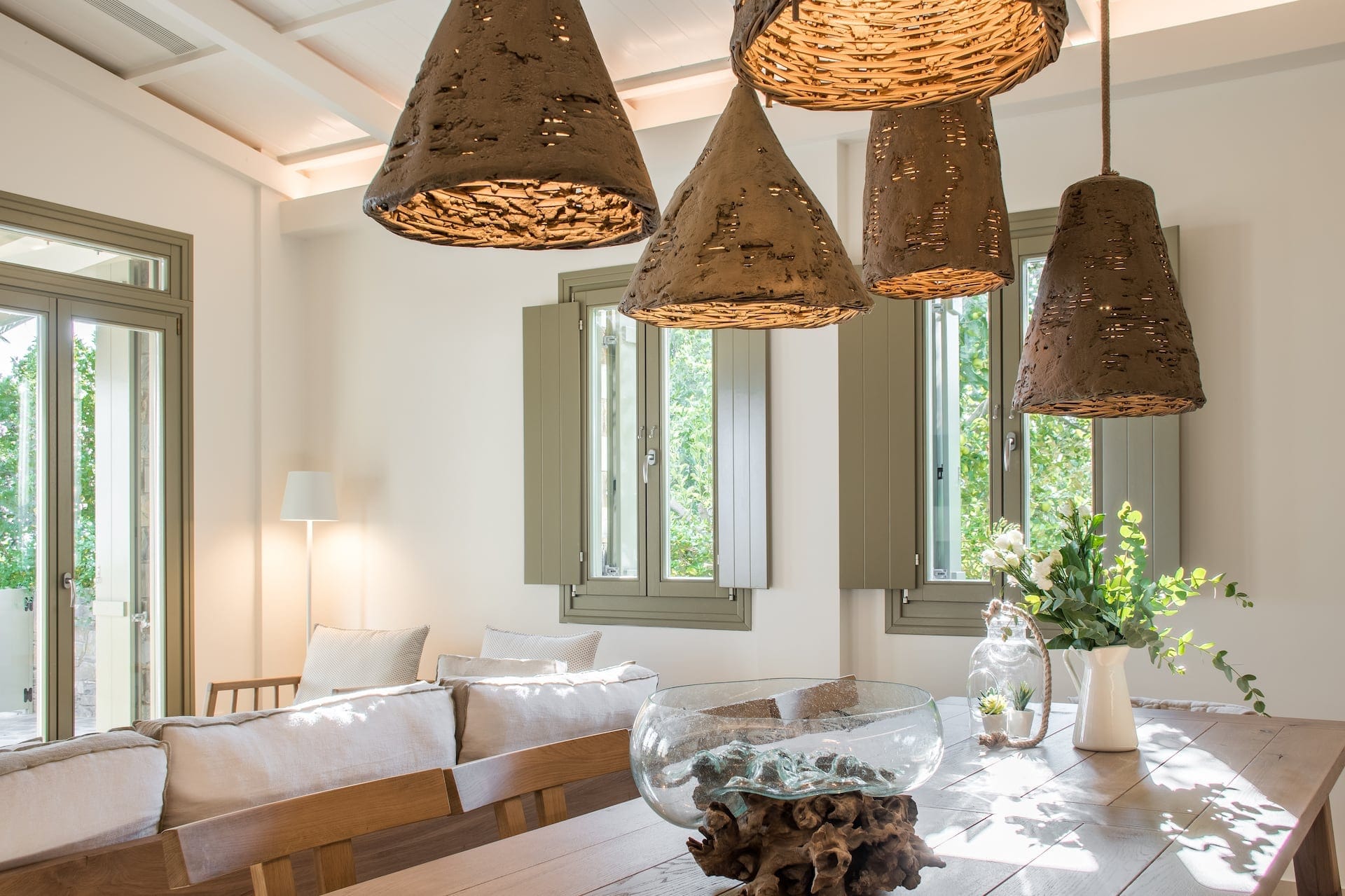 Hanging lamps over wooden dining table bathed in sunlight with vase with a plant